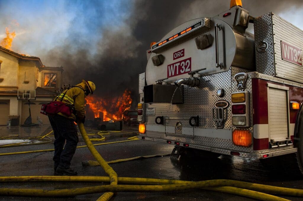 A firefighter standing next to a fire truck while putting out an active house fire.