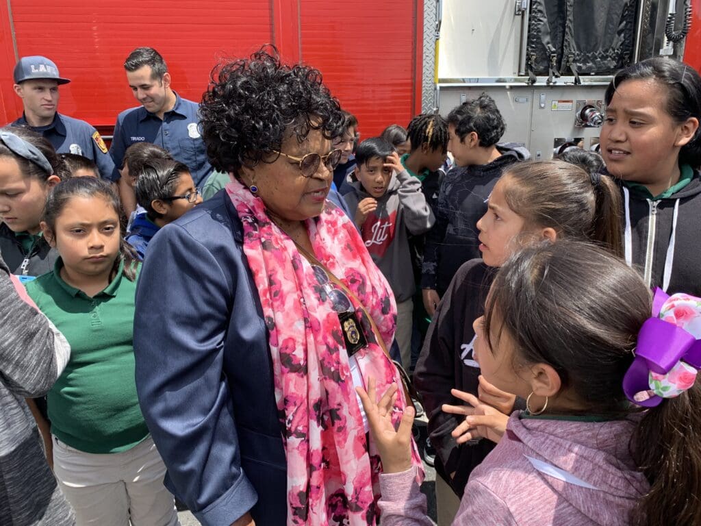 School children crowded around a female representative from MySafe:LA, with two male members from the Los Angeles Fire Department in the background.
