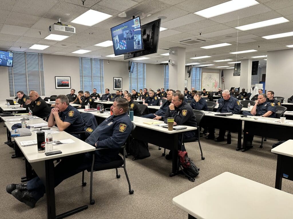 A room of safety officials and responders sitting at desks, looking at a presentation or course