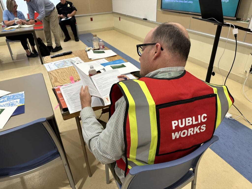 A man wearing a "Public Works" safety vest while reviewing a workbook and sitting at a desk.