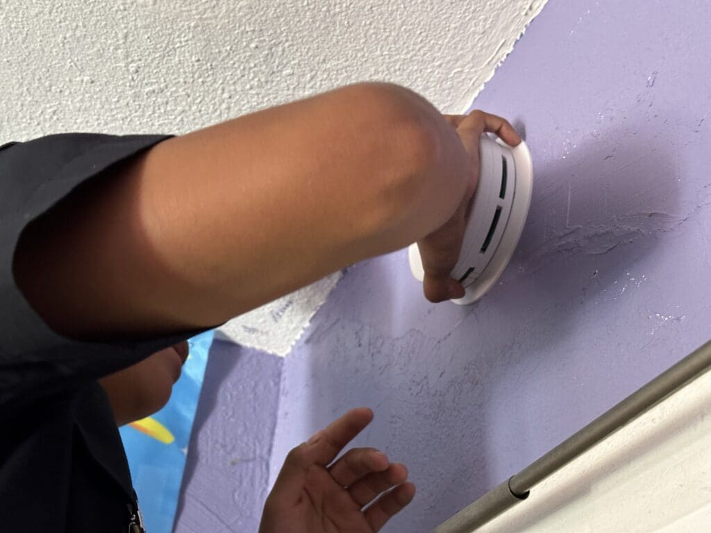 Close up image of a person installing a smoke alarm on a wall.