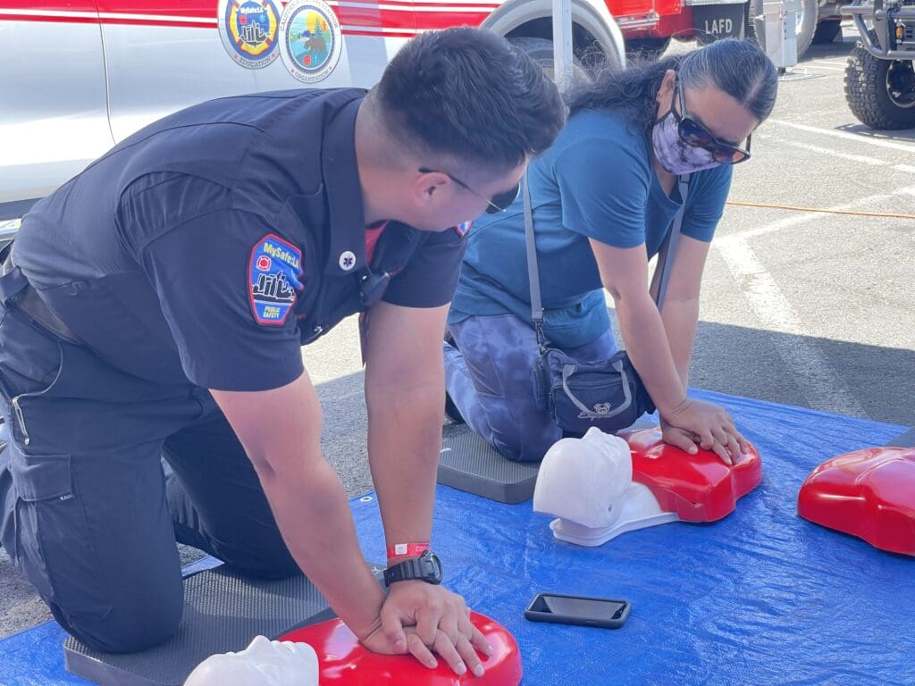 A member of MySafe:LA teaching a woman how to perform CPR on a dummy model.