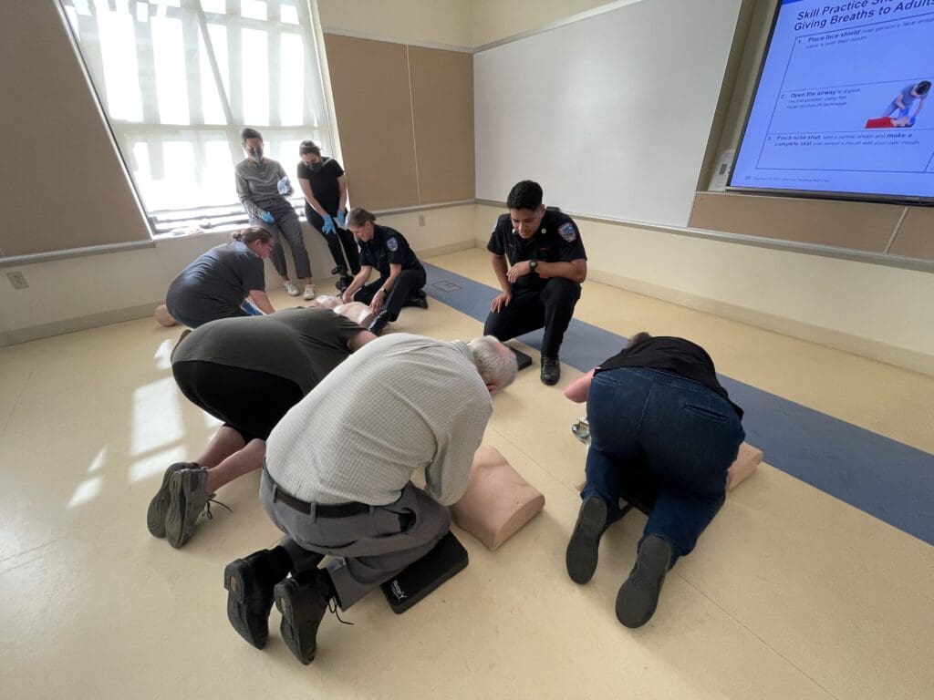 Men and women performing hands-on CPR exercises on dummy models while being supervised by members of the MySafe:LA team.